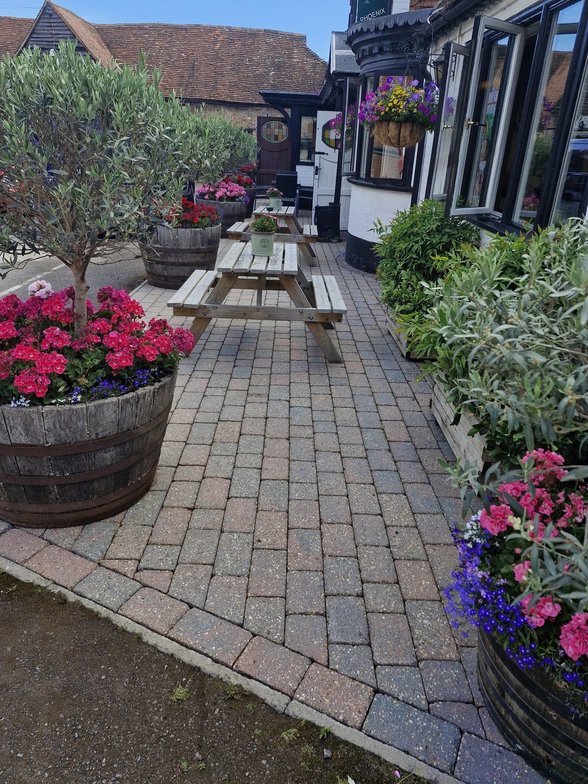 Clean block paving running between flower planters and picnic benches outside a pub.